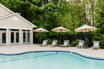 A pool with a house and four chairs with umbrellas.